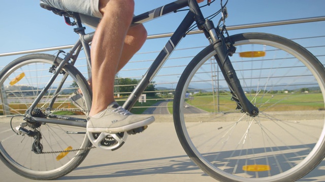 近距离观察:一个穿着牛仔短裤、面目全非的男人骑着自行车过桥。