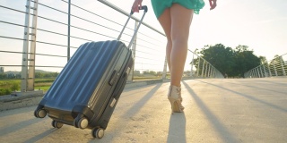 低角度:一名年轻女子穿着高跟鞋拖着她的行李箱去机场
