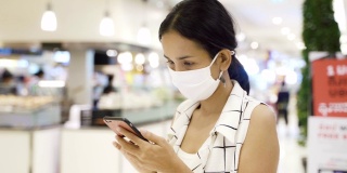 年轻的亚洲女性使用智能手机戴口罩，保护灰尘和病毒，保持健康。