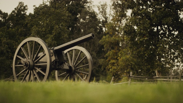 日落时分，宾夕法尼亚州葛底斯堡国家军事公园的一门美国内战大炮，在森林和木栅栏旁边的草地上