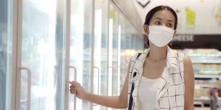 年轻的亚洲女性在超市的冷冻室里选择和挑选产品，戴上防护灰尘和病毒的面罩，保持健康。