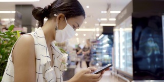 年轻的亚洲女性使用智能手机戴口罩，保护灰尘和病毒，保持健康。