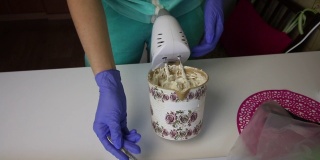 一个女人用搅拌机在一个容器里准备棉花糖。用勺子从搅拌器中取出。