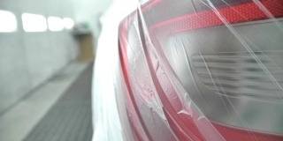 一辆白色的车正站在喷淋室里，上面覆盖着一层透明的薄膜。准备油漆。尾灯