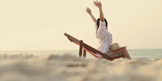 年轻的亚洲女性伸展双臂举起感觉放松躺在沙滩上的躺椅上。夏天度假的概念。