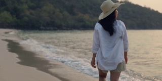 肖像快乐微笑的亚洲女性走在海滩美丽的日落。生活方式旅游度假夏季概念。