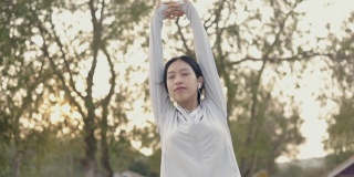 亚洲女子运动员听音乐穿着运动服伸展双臂举起感觉放松慢跑健康的生活方式锻炼在海边在日出。