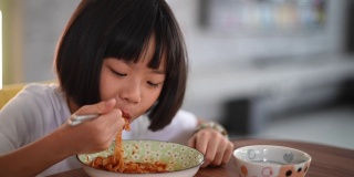 一个亚洲华裔的小女孩在家做了面条，在餐厅用筷子吃
