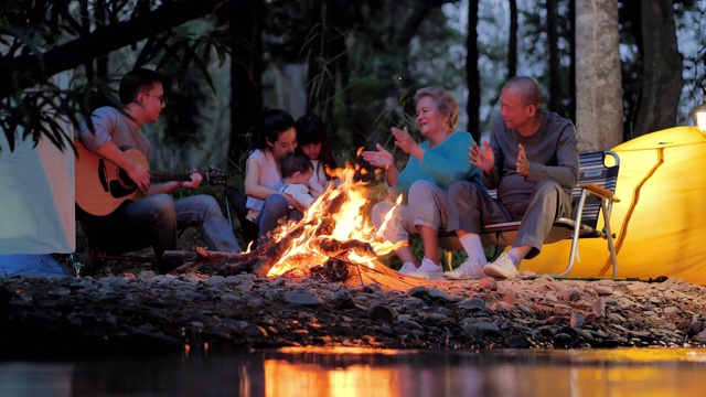 快乐的亚洲大家庭享受在森林篝火附近的夜晚露营。家庭，生活方式，人，多代人，老年人，假期，关系，假期，退休，保健和医学概念。东南亚及东亚:世代家庭