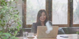 一个亚洲女人一边用笔记本电脑工作一边喝咖啡