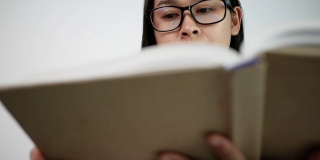 一名年轻女子在图书馆看书时翻动书页，手指在书页上移动。有选择性的重点。