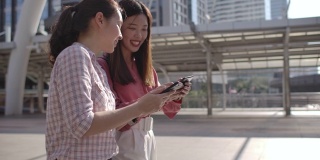 在城市里和朋友一起走路和使用智能手机的亚洲女人
