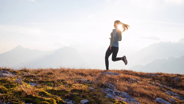 健康的女性运动员保持健康的生活方式，在日落时在岩石小径和草坡上跑步