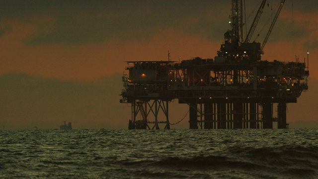 在一个戏剧性的，暴风雨的天空下的日落在前景与海浪的地平线上的几个近海石油钻井平台的慢动作拍摄