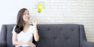 亚洲女性用画问号来做决定，有一个想法并指向灯泡，解决方案和发现，象征灯泡代表智慧和灵感，天才代表成功的概念。
