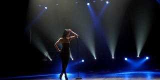 在蓝色聚光灯下，一个美丽的歌手在黑暗的舞台上摆姿势。