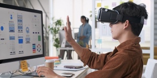 年轻的亚洲设计师使用虚拟现实眼镜(虚拟现实)测试手机应用程序开发与桌面电脑在现代创意办公室
