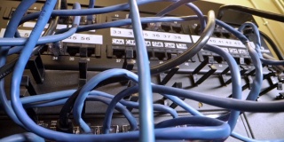 在IT组网柜背景中，Cat5e以太网线缆插入交错的、杂乱的高速千兆因特网Cat5数据补丁线缆闪烁的网络交换机