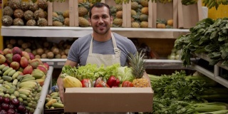 一名友善的男子正准备在一个装满新鲜水果和蔬菜的纸箱里为顾客送货，微笑着看着相机