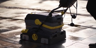 清洁工使用手动电动推式清扫车，在室外用湿式热压清洗机清洗城市人行道铺路板。道路清扫机详情。检疫卫生措施