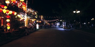 越南广南会安- 2020年3月8日:时间推移。人们走在古老的古城会安附近的图邦河，中国传统灯笼装饰着咖啡馆和餐馆。联合国教科文组织世界遗产。