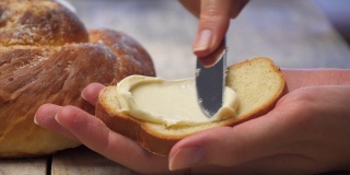 一位女性的手用一把刀在白面包上抹黄油。