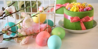 春节复活节餐桌。小的绿色蛋糕，背景上有奶油花和五颜六色的鸡蛋。五颜六色的复活节彩蛋在桌子上滚动