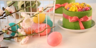 春节复活节餐桌。小的绿色蛋糕，背景上有奶油花和五颜六色的鸡蛋。女人手里拿着一个彩色的复活节彩蛋放在篮子里