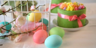春节复活节餐桌。小的绿色蛋糕，背景上有奶油花和五颜六色的鸡蛋。女人伸手把一个盛着蛋糕的盘子放在桌子上