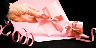 女手将带粉红丝带的礼品盒放在粉黑背景上