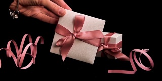 女手将带粉红丝带的礼品盒放在粉黑背景上