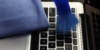 一个戴着橡胶手套的男人正在清洁他的笔记本电脑。一种特殊的刷子可以清除键盘和笔记本电脑屏幕上的灰尘。保护工作设备免受病毒感染。
