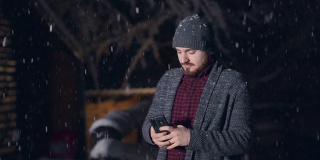随着雪花从天空飘落，帅气的年轻人正在用手机发短信。股票视频