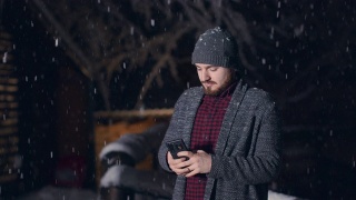 随着雪花从天空飘落，帅气的年轻人正在用手机发短信。股票视频视频素材模板下载