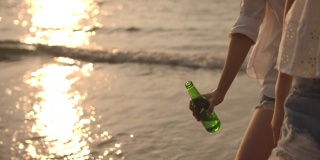 慢动作的手在日落的海滩上敬啤酒瓶，胜利，庆祝