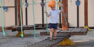 婴儿在街上的一个绳子小镇上玩。一个男孩走在儿童器材上摔倒了。一个孩子在操场上走在摇摇欲坠的木桥上。