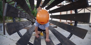 婴儿在一个绳子小镇玩。男孩爬进了儿童器材里。一个孩子在操场上的桥上爬行。