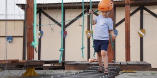 婴儿在街上的一个绳子小镇上玩。一个男孩在儿童器材上行走。一个孩子在操场上走在摇摇欲坠的木桥上。
