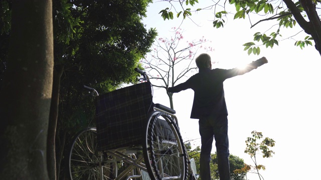 坐在轮椅上的亚洲老人在公园户外伸展双臂