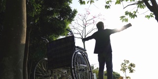 坐在轮椅上的亚洲老人在公园户外伸展双臂
