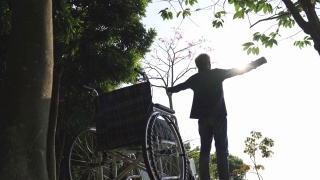 坐在轮椅上的亚洲老人在公园户外伸展双臂视频素材模板下载