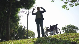 亚洲老人从户外公园的轮椅上站起来视频素材模板下载