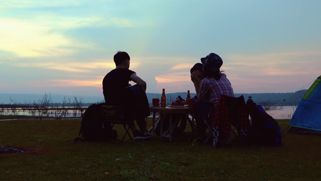 一群亚洲朋友在夏天一起喝酒和弹吉他，在日落时分在湖边露营