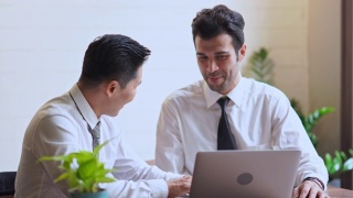 商人和合作伙伴一起讨论在笔记本电脑上的业务表现视频素材模板下载