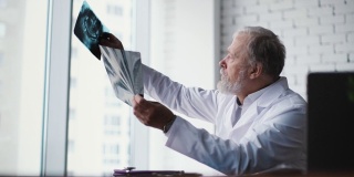 成年男性医生在一张靠大窗户的桌子前检查x光和核磁共振扫描