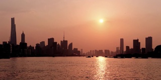 时间流逝镜头在上海城市日落与外滩天际线和黄浦江背景，货船在河上航行，太阳下降到地平线，4k视频。