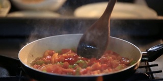 用平底锅煎西红柿和辣椒，准备饭菜，用搅拌勺搅拌食物