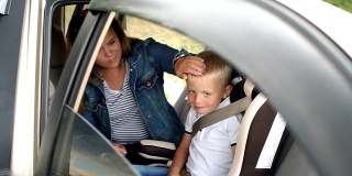 特写的母亲系她的小儿子在汽车座椅上的安全带在汽车里。