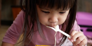 亚洲小女孩有乐趣吃面条在塑料杯在家里。垃圾食品的概念。