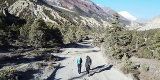 一对夫妇在尼泊尔喜马拉雅山脉的马南谷的一条森林小径上散步。安纳普尔纳的尖峰和贫瘠的山峰在后面。安纳普尔纳峰电路长途跋涉。大自然的美。尘土飞扬的道路。